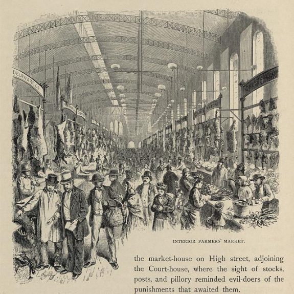 A black and white illustration of a crowd of shoppers inside of a public market shed. Meats and other produce are on display along the walls.