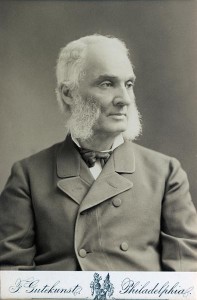 A black and white photograph of man from the chest up, wearing a jacket and a tie. 